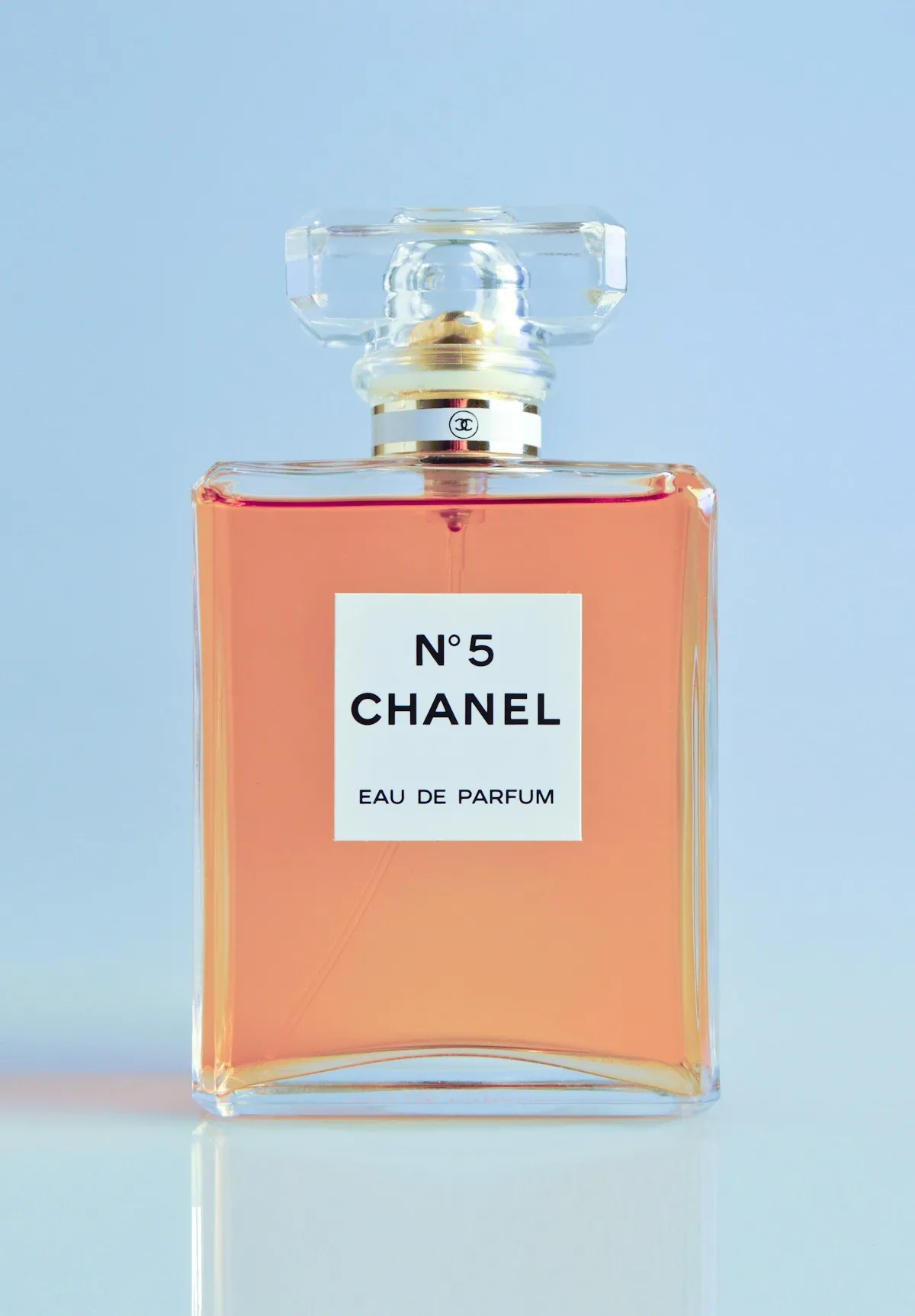 A glass perfume bottle against a pastel blue background